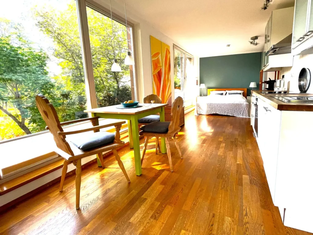 Atelier 2: Essplatz am Eckfenster, dahinter Bett und Küchenzeile in einem durchgehenden Raum